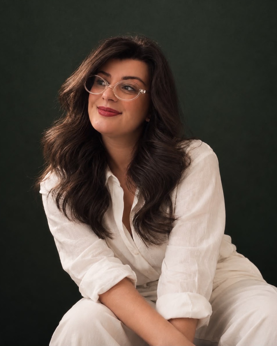 Nattália Silveira, de camisa branca e óculos, sorrindo, sobre fundo verde-escuro